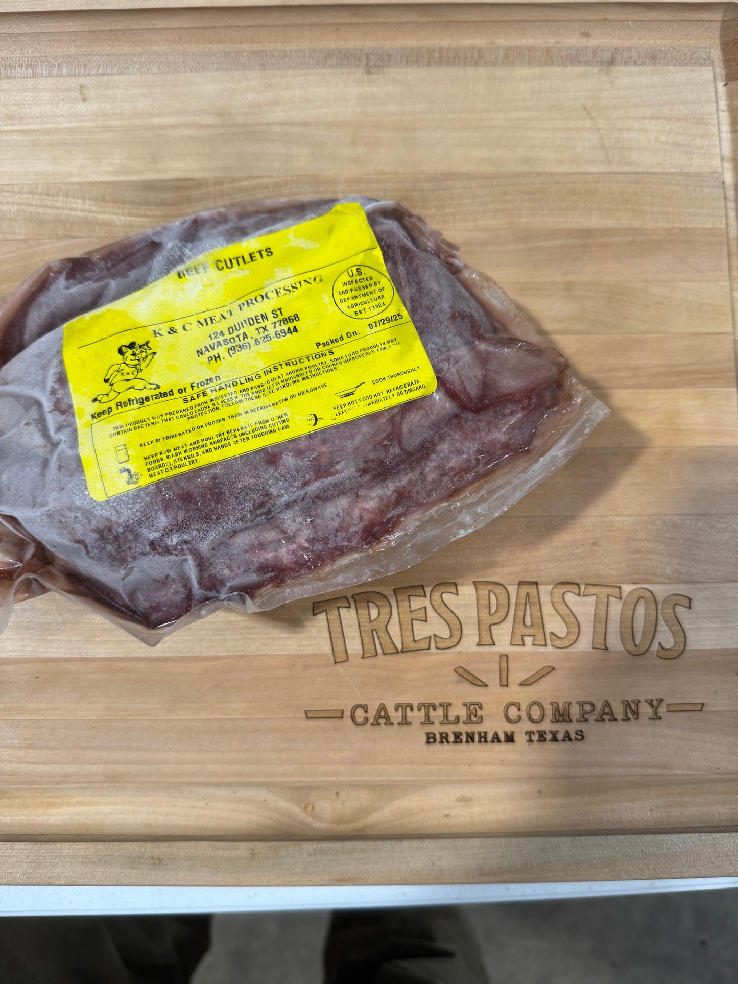 Packaged meat with a yellow label on a wooden cutting board with 'Tres Pastos Cattle Company' branding.